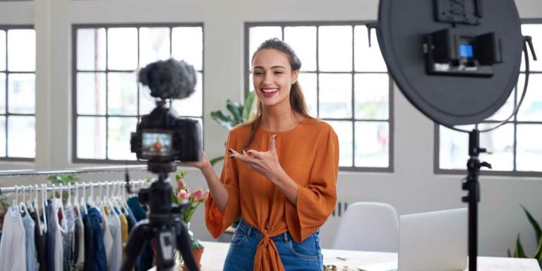 Una ragazza come influencer parla davanti una telecamera e ha alle spalle una serie di abiti per la sua attività di influencer marketing a favore di un brand.