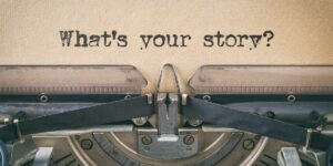 Primissimo piano di un foglio in unna vecchia macchina da scrivere, con la scritta "What's your story?", a rappresentare l'inizio di uno storitelling della mission aziendale per startup o piccole imprese.